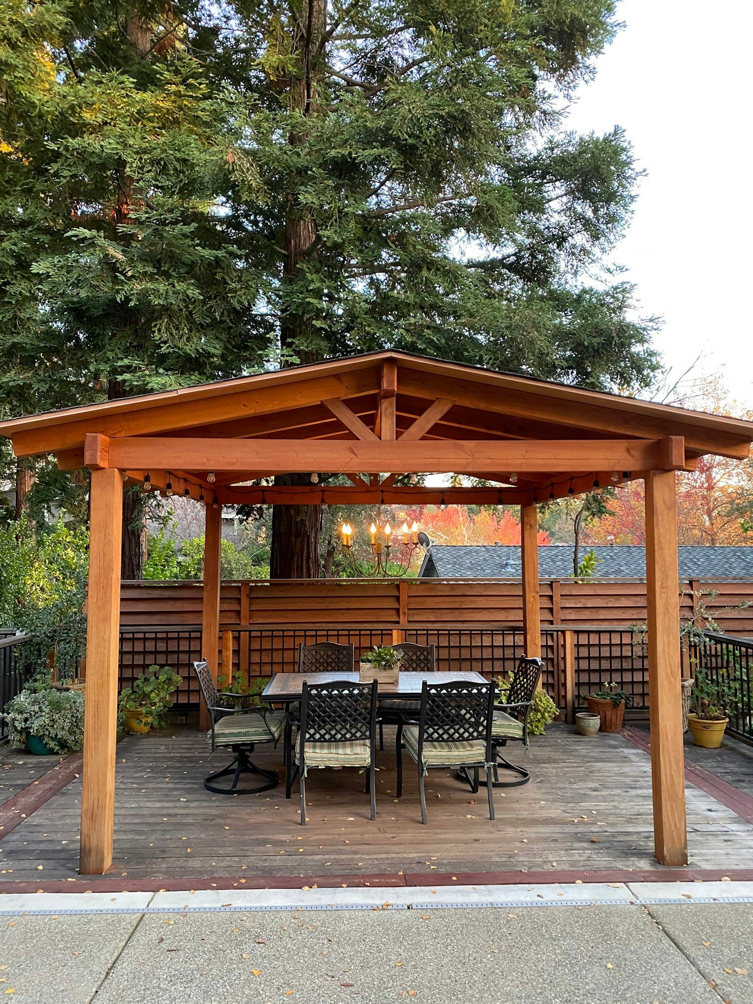 A chandelier hangs under a backyard pergola designed for luxury dining and outdoor entertainment